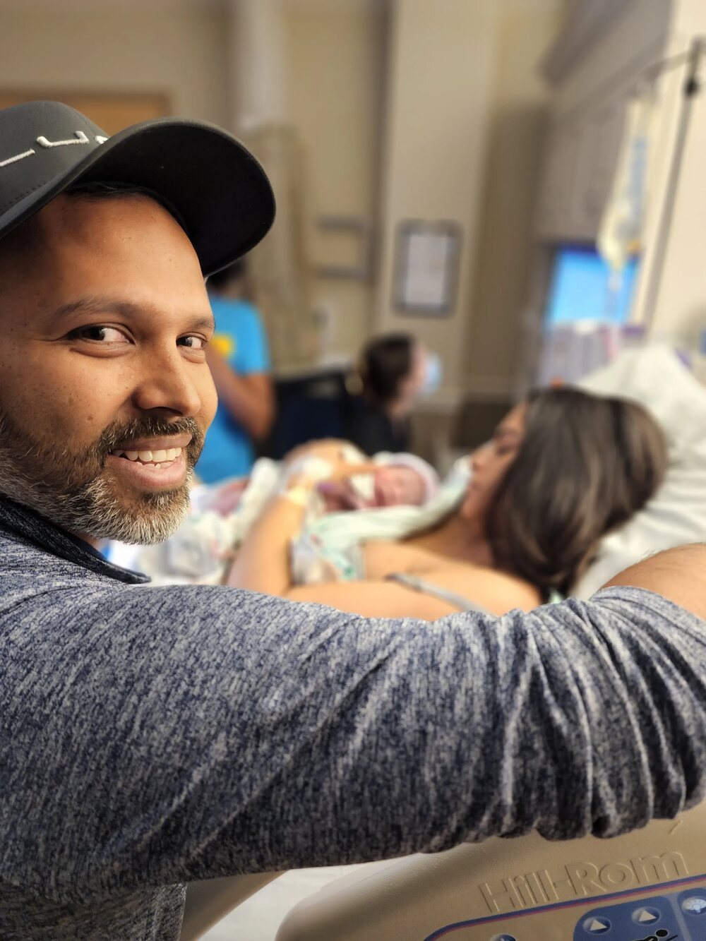 Father smiling beside mother and newborn in the birthing room