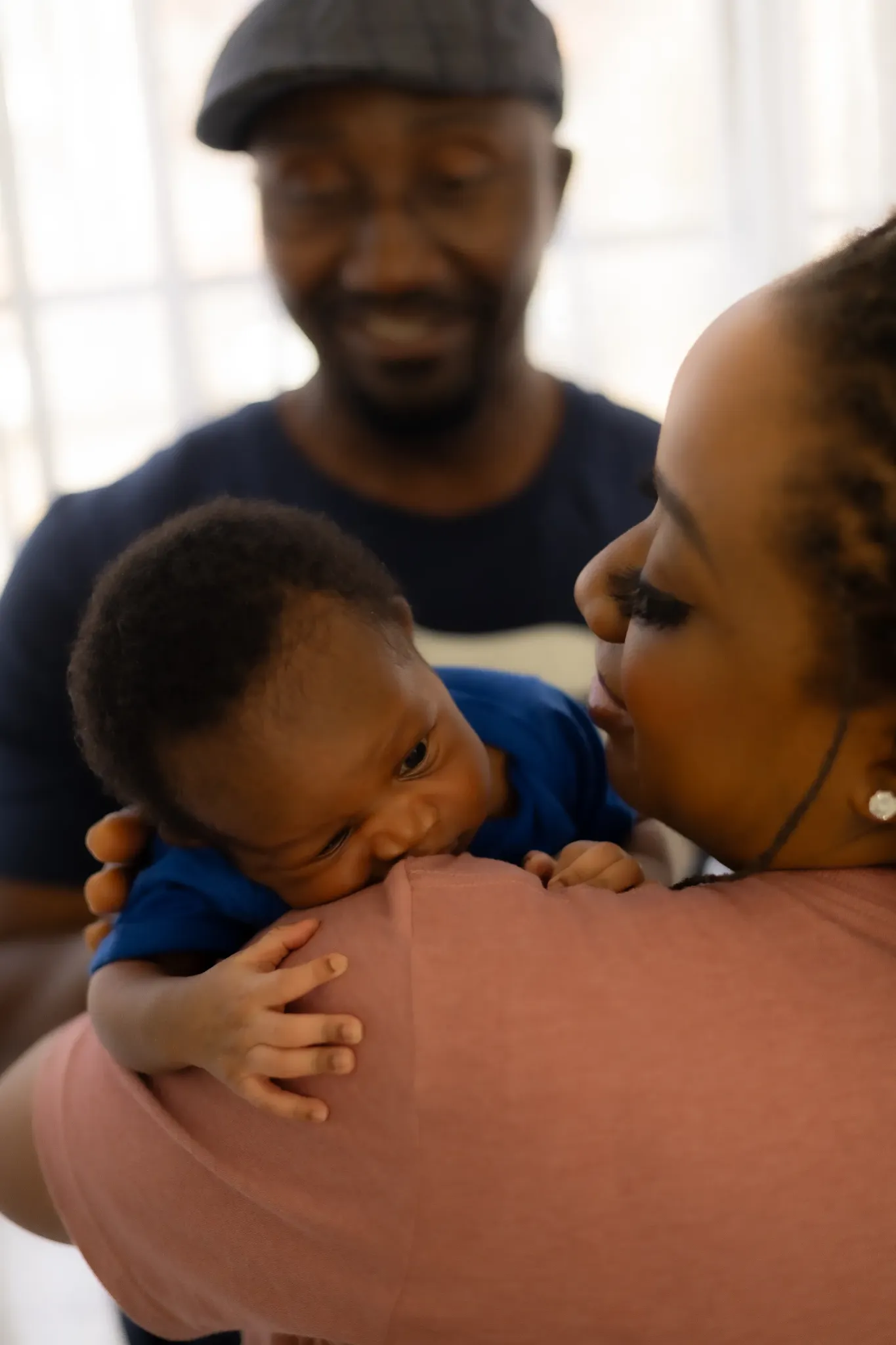 Mother cuddling baby at home while father smiles in the background